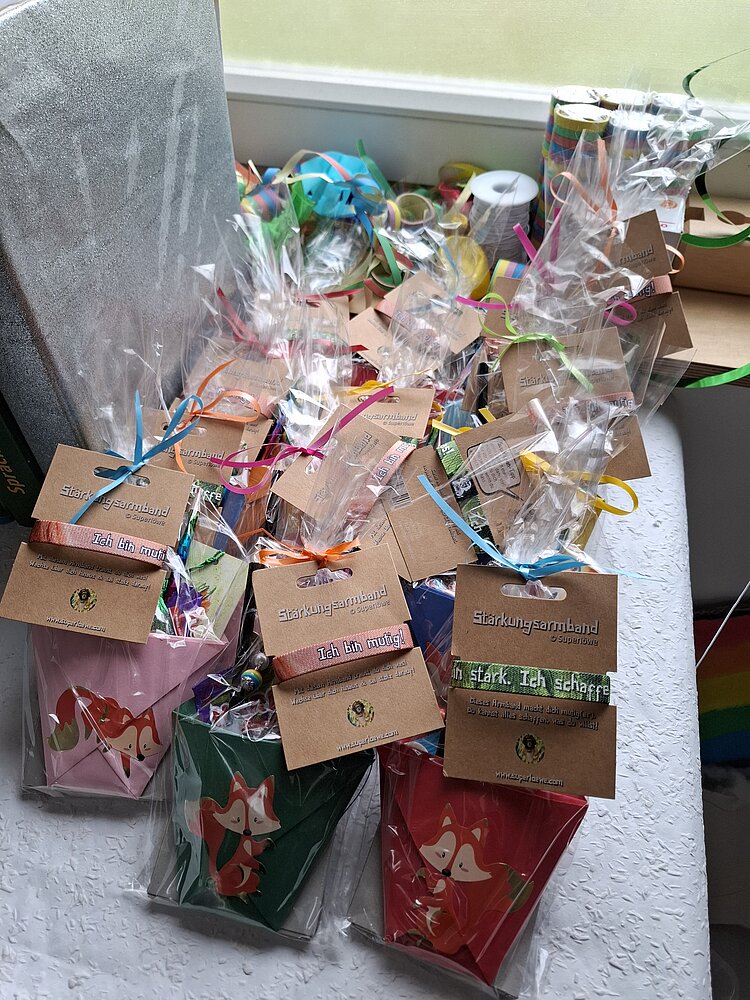 Abschiedsfest der Zaunkönige und Möwen Viele kleine Geschenktütchen mit Füchsen und bunten Armbändern, verpackt in Zellophan und dekoriert mit Bändern. Die Armbänder tragen motivierende Aufschriften wie ‚Ich bin mutig‘ oder ‚Ich bin stark. Ich schaffe das.‘ – vorbereitet als Abschiedsgeschenke für Kinder.