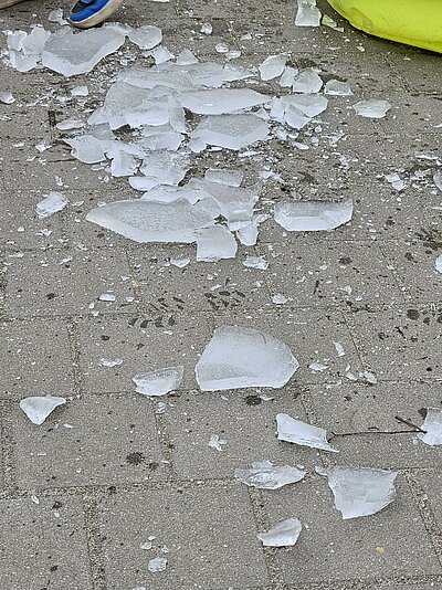 Auf einem grauen Steinboden liegen zerbrochene Eisschollen, am Rand ist ein blauer Kinderschuh zu sehen.