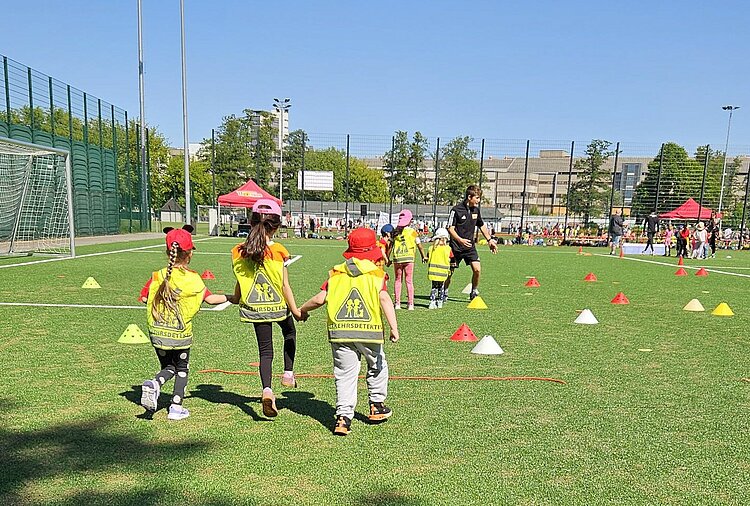Festspiele mit Ritter Keule beim 1. FC Union Berlin Kinder in Sicherheitswesten und Hüten spielen auf einem Sportfeld mit bunten Markierungskegeln.