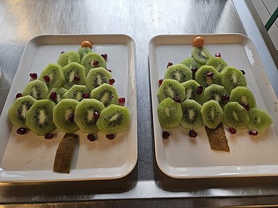 Obst in Form von Weihnachtsbäumen aus Kiwischeiben, dekoriert mit Granatapfelkernen auf weißen Tellern.