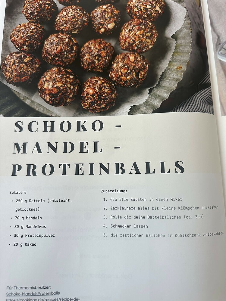 Auf der Fotografie ist im unteren Bereich das Rezept von Schoko-Mandel-Proteinballs festgehalten. In der oberen Hälfte sieht man ein Foto der gesunden Leckerei.