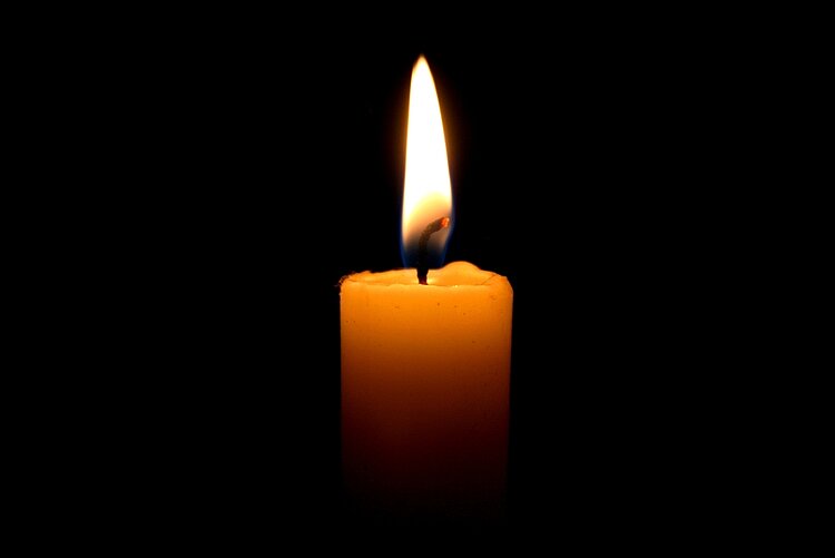 Eine weiße Kerze brennt vor schwarzem Hintergrund.