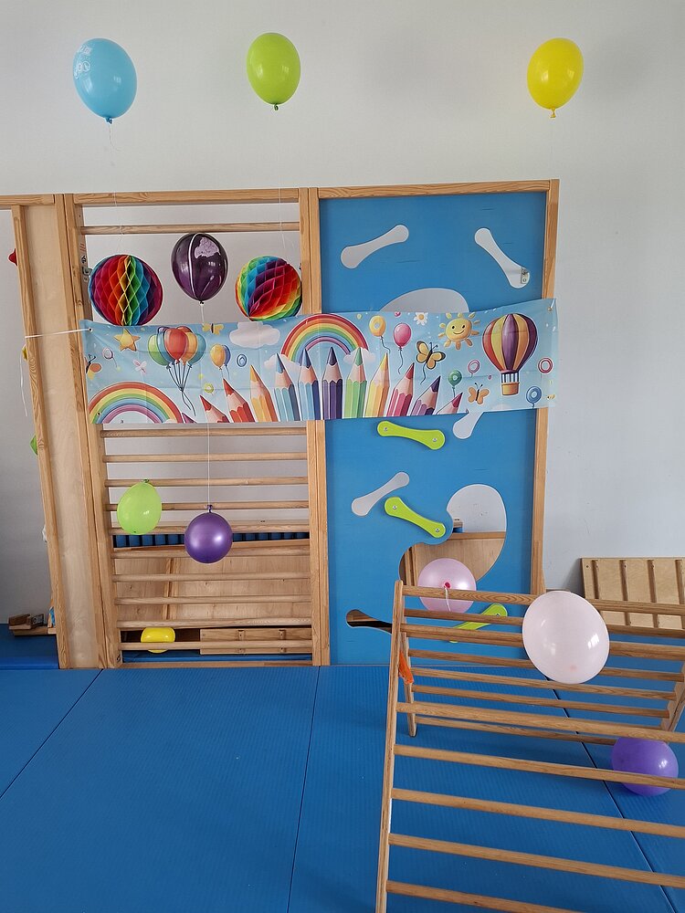 Abschiedsfest der Zaunkönige und Möwen Ein Klettergerüst im Innenraum ist festlich mit bunten Luftballons, Papierdekorationen und einem Banner mit Regenbögen und bunten Buntstiften geschmückt – eine fröhliche Dekoration für ein Kindergartenabschiedsfest.