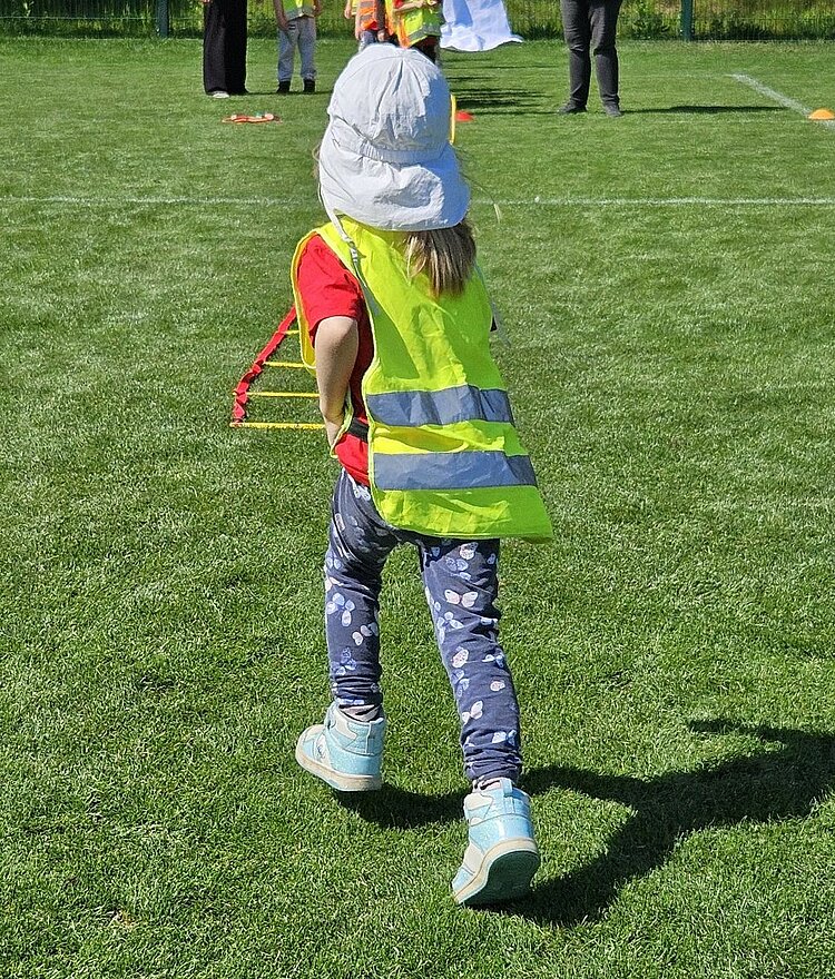 Festspiele mit Ritter Keule beim 1. FC Union Berlin Ein Kind mit einem weißer Sonnenkappe und einer gelben Sicherheitsweste läuft auf einem grünen Sportrasen.