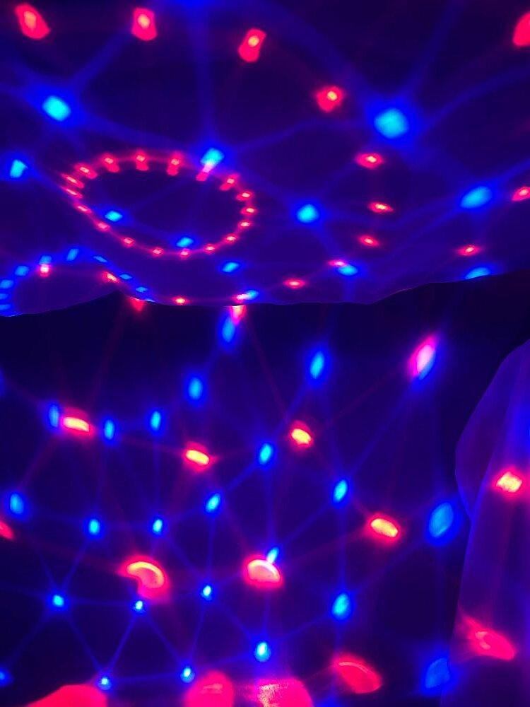 Bunte Lichter in Pink, Violett und Blau auf aufgehängten Stoffen, die von einer Diskokugel erzeugt werden.