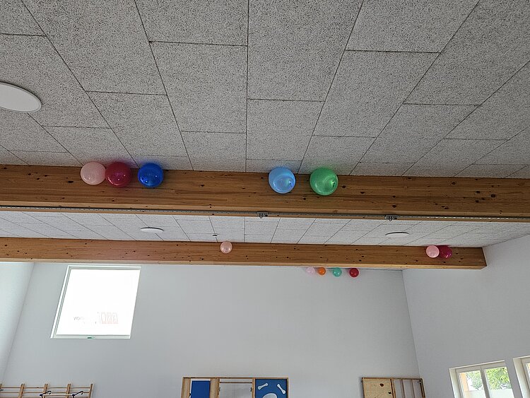 Ein unvergessliches Kita-Abenteuer: Unsere Übernachtung voller Magie und Gemeinschaft Neben den Holzbalken eines Sportraums hängen ganz oben an der Decke bunte Ballons, die mit Helium gefüllt sind.