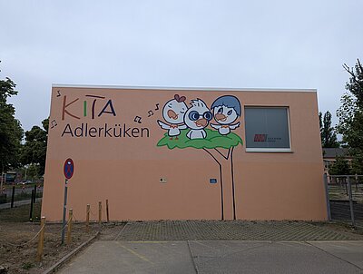 Wir können uns sehen lassen! Eine Hauswand, auf der das Logo der KITA Adlerküken zu sehen ist in Form eines Graffitis