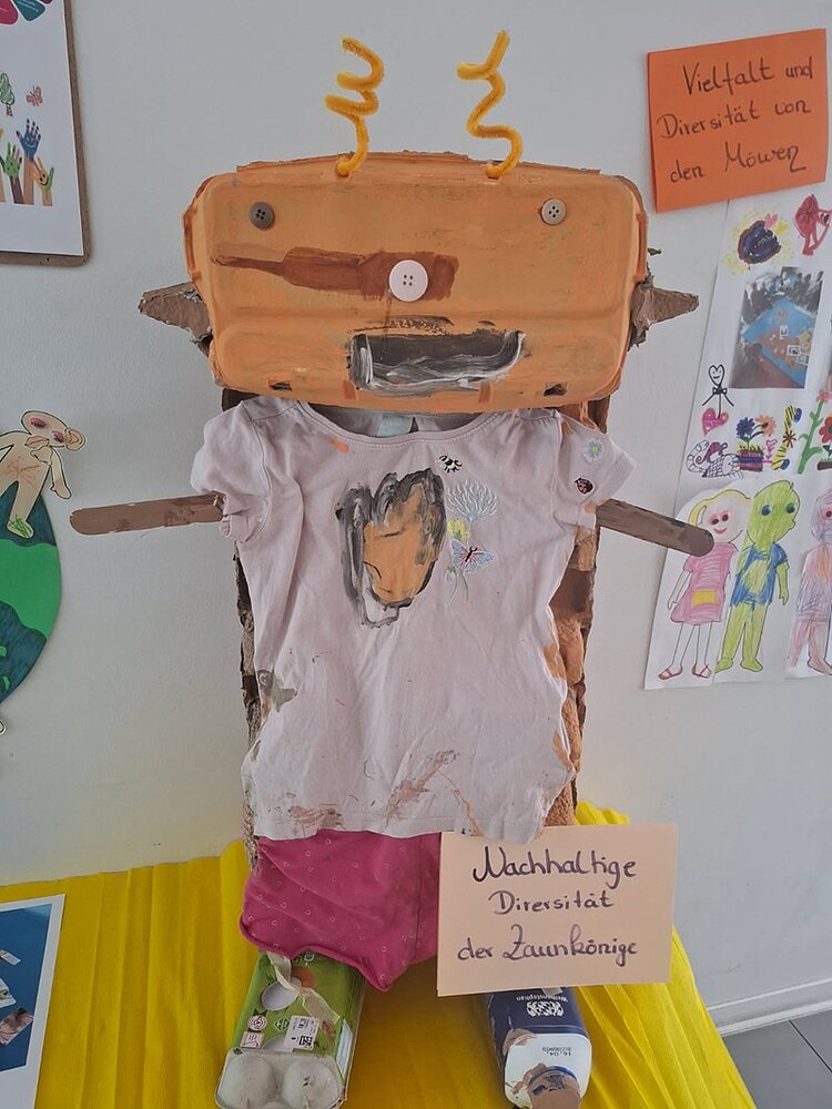 Tag der Diversität an der KITA Adlerküken Ein von den Kita-Kindern selbst gestaltete nachhaltige Figur, auch Pappkartons, mit Pfeifenreinigern als Fühler, einem alten T-Shirt, mit Knöpfen als Augen und Nase, Füßen aus einem Tetra-Pak und einem Eierkarton.