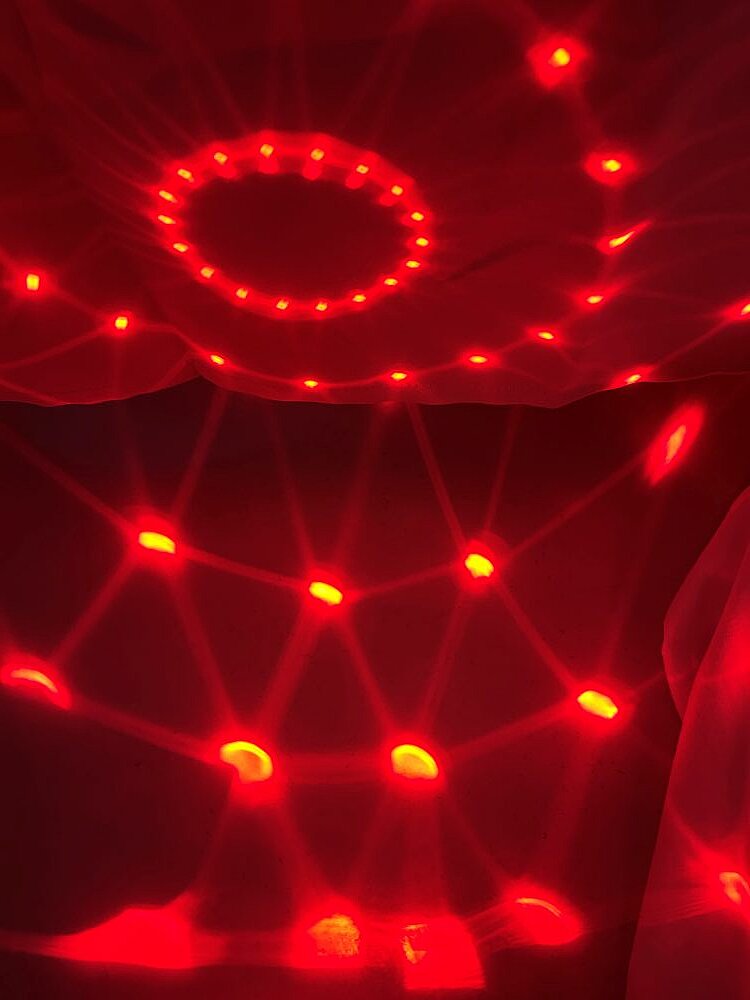 Lichter in verschiedenen Rottönen auf hängenden Tüchern, die von einer Diskokugel erzeugt werden.