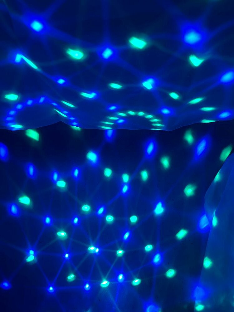 Bunte Lichter in Blau und Grün auf hängenden Tüchern, die von einer Diskokugel erzeugt werden.