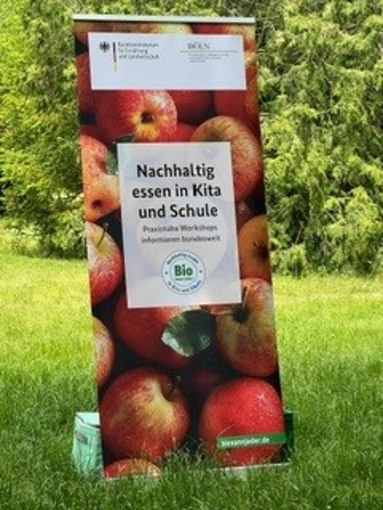 An einen Baum gelehnt steht ein Schild mit Äpfeln abgebildet.